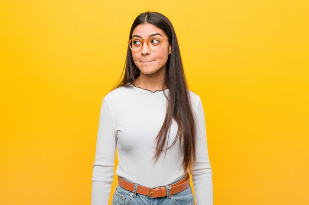 Giovane bella donna araba contro un muro giallo confuso, si sente dubbioso e incerto.