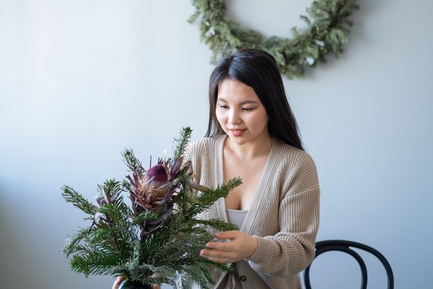 Giovane bella donna asiatica che decora la tavola con i rami dell'albero di Natale e le candele