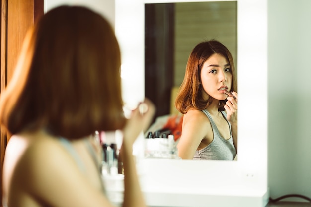 Giovane bella donna asiatica che fa trucco vicino allo specchio