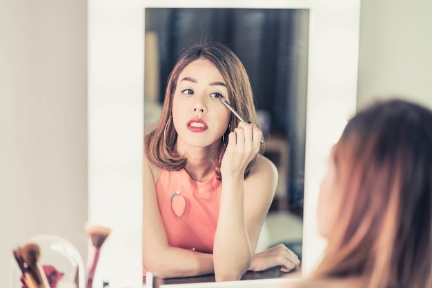 Giovane bella donna asiatica che fa trucco vicino allo specchio