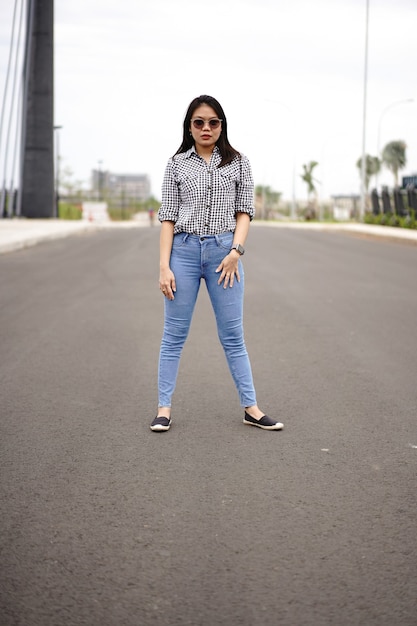 Giovane bella donna asiatica che indossa camicia a quadri e jeans blu in posa all'aperto