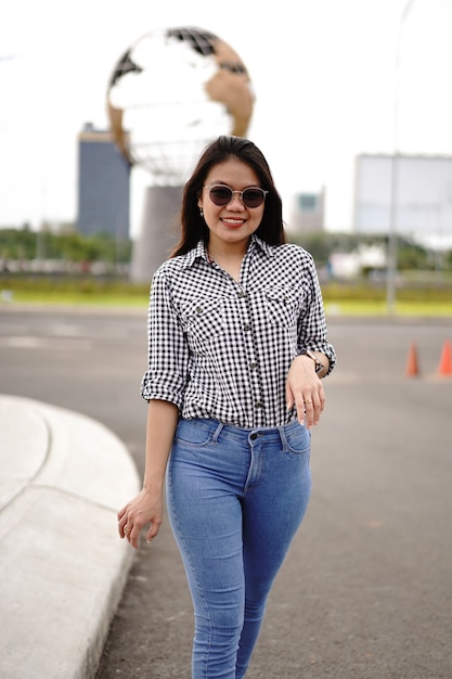 Giovane bella donna asiatica che indossa camicia a quadri e jeans blu in posa all'aperto