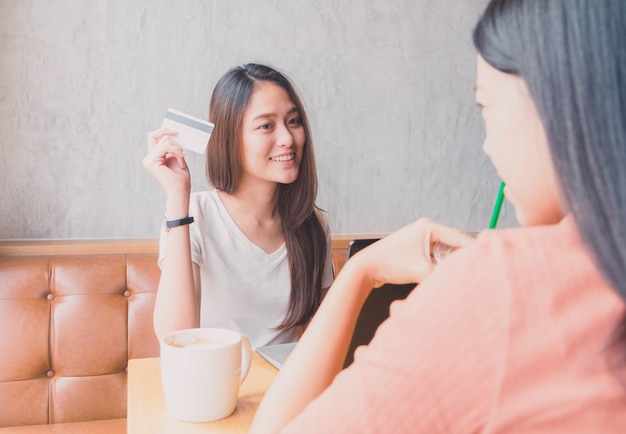 Giovane bella donna asiatica che parla e che compera con la carta di credito nel fondo della caffetteria