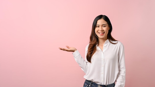 Giovane bella donna asiatica che si diffonde puntando le mani da parte su sfondo rosa isolato