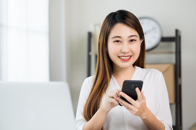 Giovane bella donna asiatica di affari che utilizza smartphone. Sorridente affascinante felice giovane femmina sms toccando sul display del telefono cellulare.