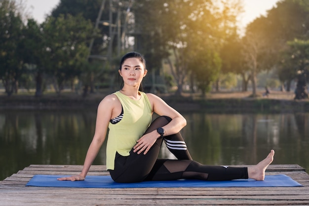 Giovane bella donna asiatica in abiti sportivi che fa yoga all'aperto nel parco al mattino con una calda luce solare per uno stile di vita sano. Yogi di giovane donna che fa yoga nel parco mattutino