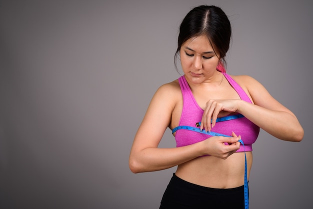 Giovane bella donna asiatica pronta per la palestra contro il muro grigio