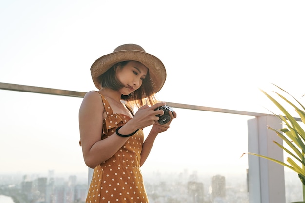 Giovane bella donna asiatica viaggiatrice che utilizza una fotocamera digitale compatta e sorride