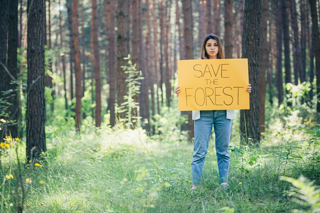 Giovane bella donna attivista volontaria nella foresta con un poster salva la foresta