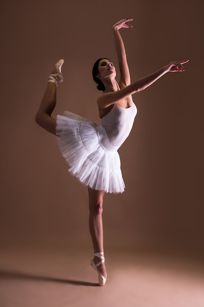 Giovane bella donna ballerina in tutu in posa sulle dita dei piedi su sfondo beige