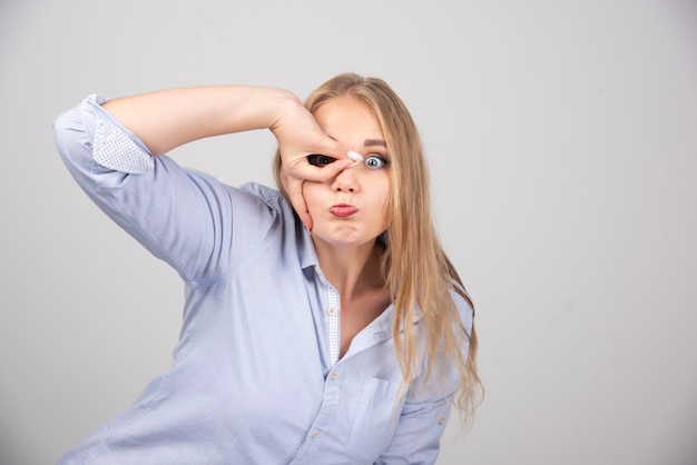 Giovane bella donna bionda che fa un gesto ok come un binocolo e guarda attraverso le dita.