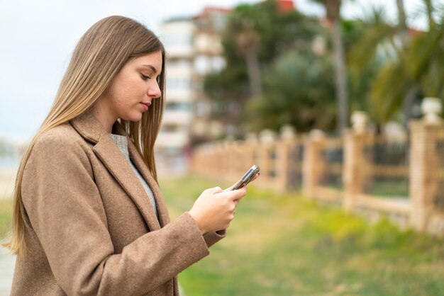 Giovane bella donna bionda che invia un messaggio o un'e-mail con il cellulare