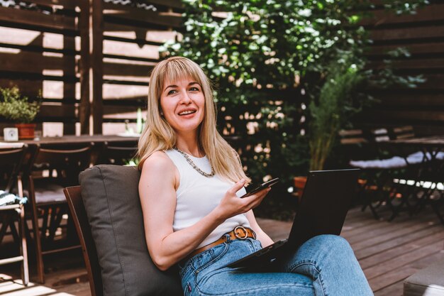 Giovane bella donna bionda che lavora al computer portatile e parla al telefono in un accogliente spazio di coworking