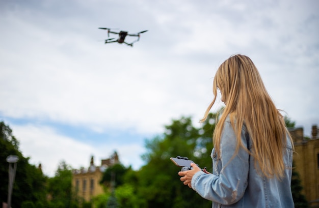 Giovane bella donna bionda che pilota un drone con un telecomando in mano