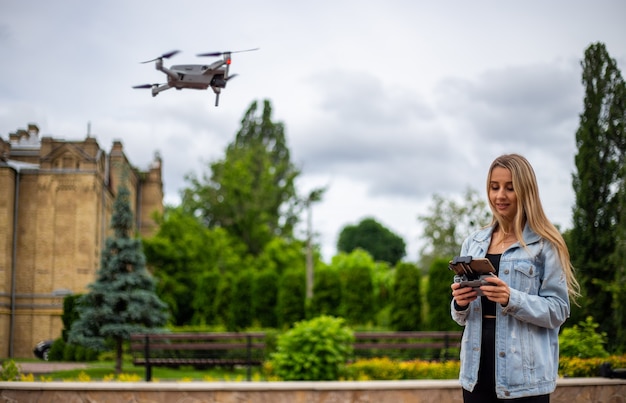 Giovane bella donna bionda che pilota un drone con un telecomando in mano