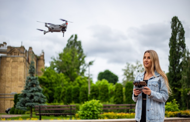 Giovane bella donna bionda che pilota un drone con un telecomando in mano