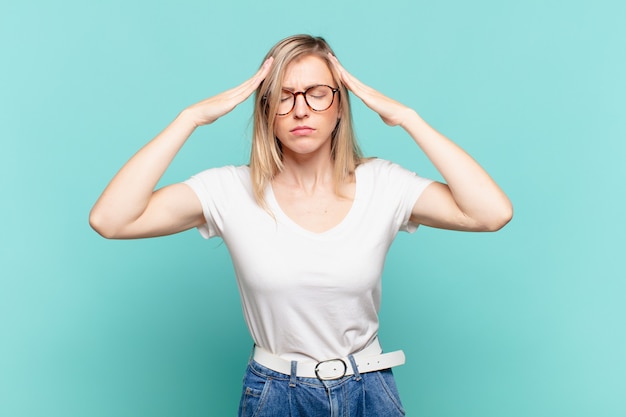 Giovane bella donna bionda che sembra concentrata, premurosa e ispirata, che fa brainstorming e immagina con le mani sulla fronte