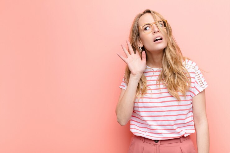 Foto giovane bella donna bionda che sembra seria e curiosa, ascoltando, cercando di ascoltare una conversazione segreta o un gossip, origliando sulla parete colorata