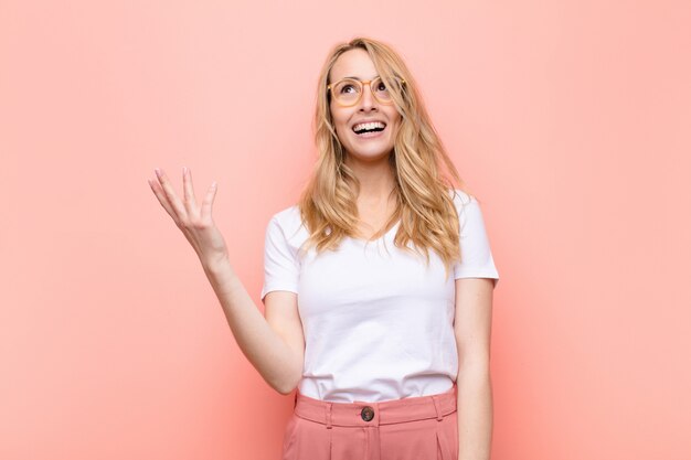 Giovane bella donna bionda che si sente felice, sorpresa e allegra, sorridente con atteggiamento positivo, realizzando una soluzione o un'idea contro la parete di colore piatto