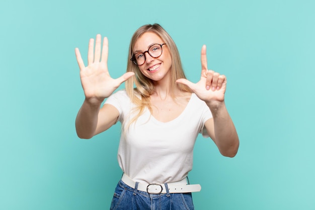 Giovane bella donna bionda che sorride e sembra amichevole, mostrando il numero sette o settimo con la mano in avanti, conto alla rovescia