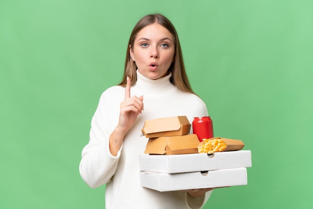 Giovane bella donna bionda che tiene cibo da asporto su sfondo isolato che intende realizzare la soluzione mentre si alza un dito