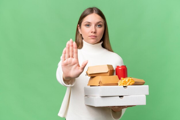 Giovane bella donna bionda che tiene cibo da asporto su sfondo isolato facendo gesto di arresto