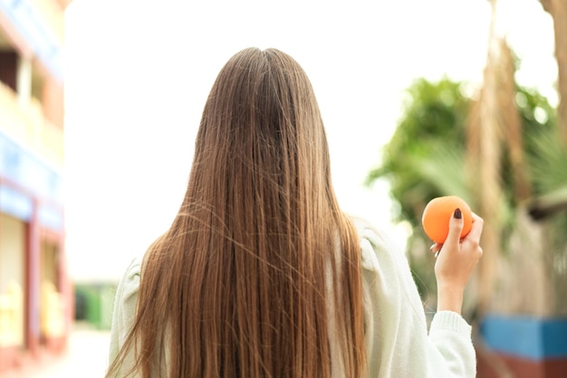 Giovane bella donna bionda che tiene un'arancia all'aperto in posizione arretrata