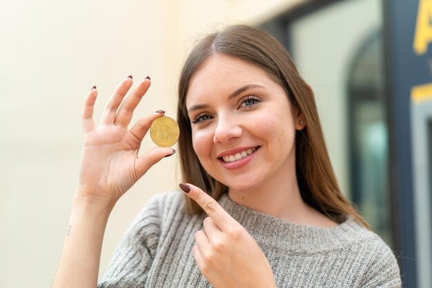 Giovane bella donna bionda che tiene un Bitcoin e lo punta