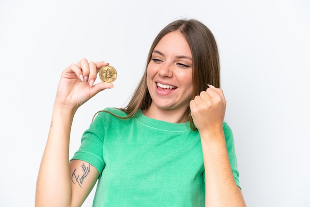 Giovane bella donna bionda che tiene un Bitcoin isolato su sfondo bianco che celebra una vittoria