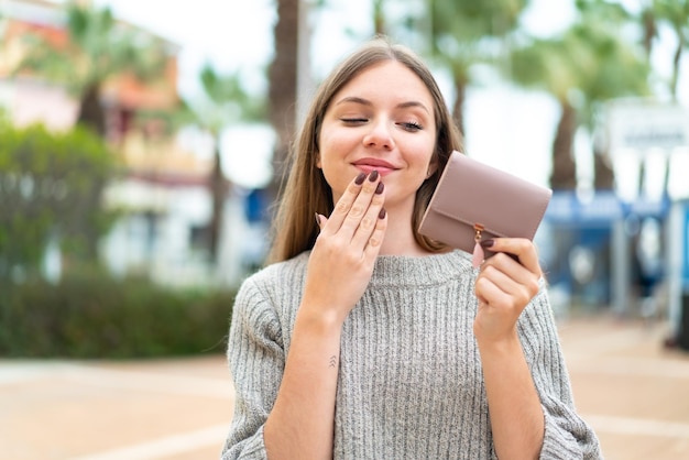 Giovane bella donna bionda che tiene un portafoglio e lo guarda