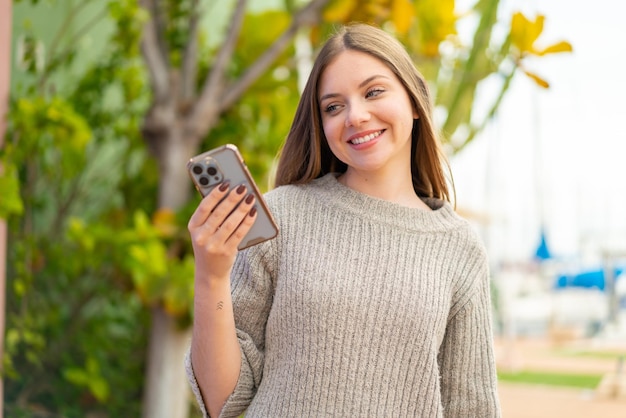 Giovane bella donna bionda che utilizza il telefono cellulare all'aperto con un'espressione felice