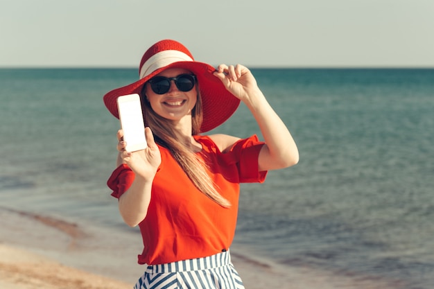 Giovane bella donna bionda con il cellulare sulla spiaggia