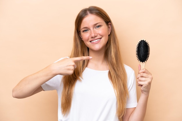 Giovane bella donna bionda con pettine per capelli isolato su sfondo beige e puntandolo