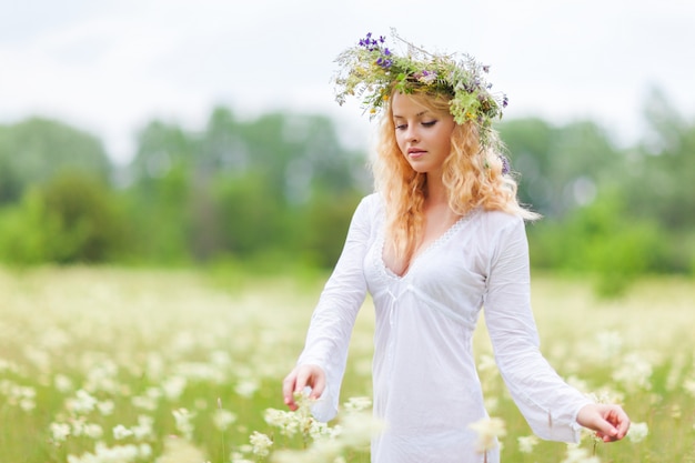 Giovane bella donna bionda in abito bianco e corona floreale