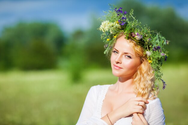 Giovane bella donna bionda in abito bianco e corona floreale