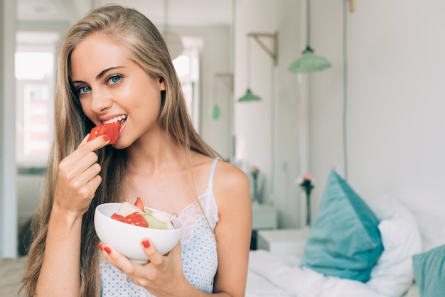 Giovane bella donna bionda in buona salute nel letto che mangia frutti