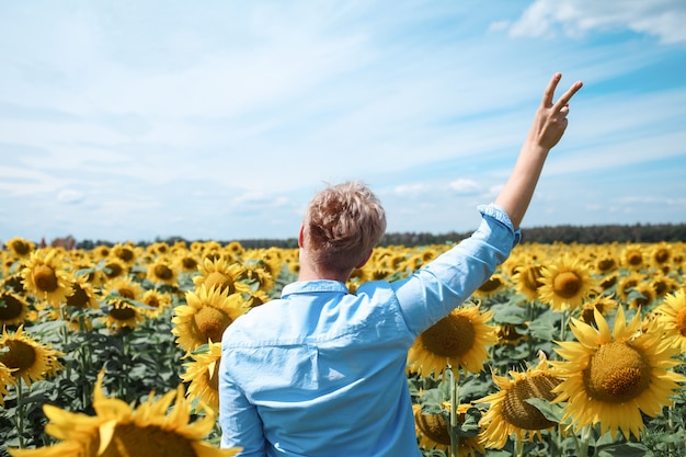 Giovane bella donna bionda in piedi nel campo di girasoli