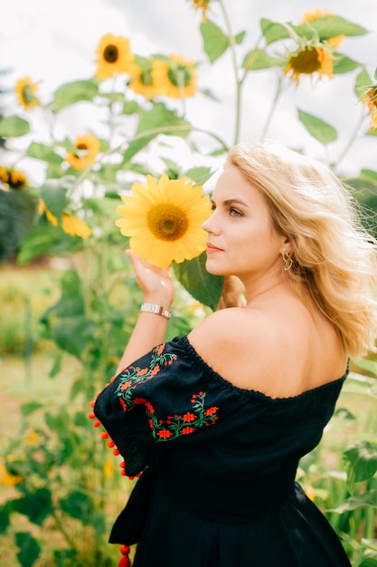 Giovane bella donna bionda in vestito nero nel giacimento del girasole