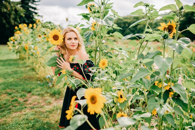 Giovane bella donna bionda in vestito nero nel giacimento del girasole