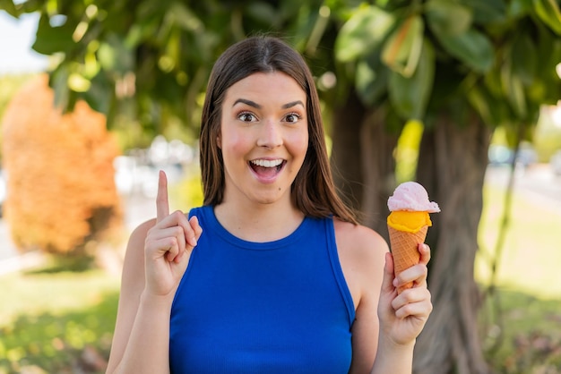 Giovane bella donna brasiliana con un gelato alla cornetta all'aperto che indica una grande idea