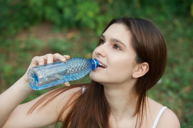 giovane bella donna bruna che beve acqua dalla bottiglia in un parco a