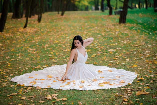 Giovane bella donna castana in un lungo abito bianco nella sosta di autunno.