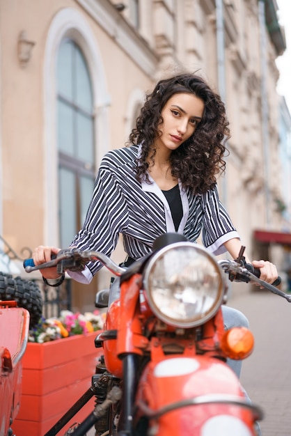 Giovane bella donna castana su una moto mentre si guida su una strada cittadina