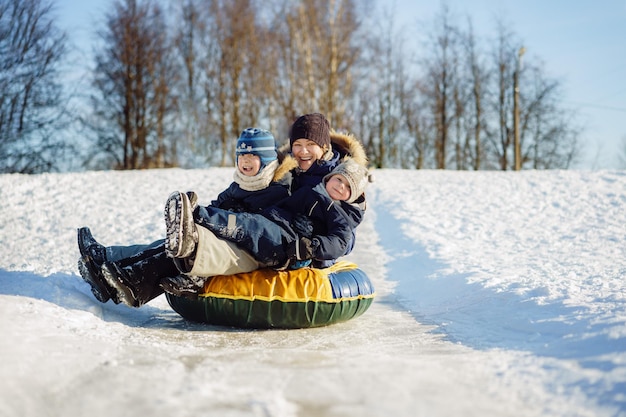 Giovane bella donna caucasica con due simpatici ragazzi che slittino lungo il pendio ghiacciato nel parco su snow tubing