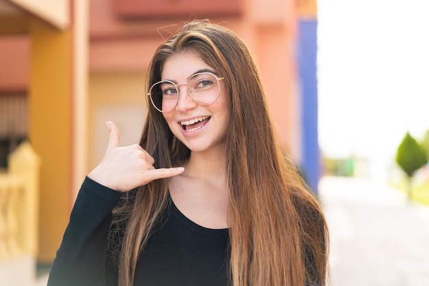 Giovane bella donna caucasica con gli occhiali e che fa il gesto del telefono