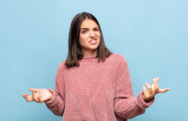 Giovane bella donna che alza le spalle con un'espressione stupida, pazza, confusa, perplessa, sentendosi infastidita e senza tracce