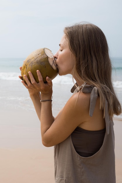 Giovane bella donna che beve acqua di cocco fresca da noce sulla spiaggia in una calda giornata di sole