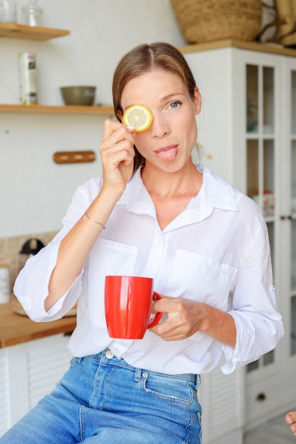 giovane bella donna che beve il tè in cucina con il limone