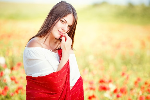 Giovane bella donna che cammina attraverso un campo di papaveri in estate. Close up ritratto di bella giovane donna romantica in posa sul campo. Colori tenui.