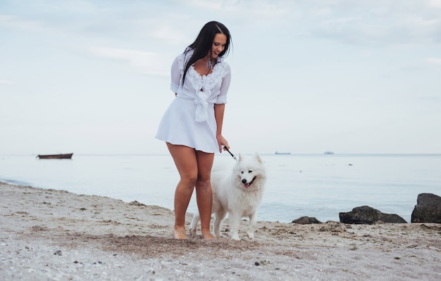 Giovane bella donna che cammina con il suo cane sulla spiaggia